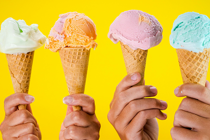 Four hands on a yellow background holding colorful ice cream cones.